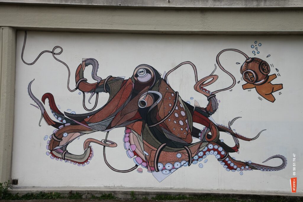 Street art de Teuthis représentant une grande pieuvre mécanique peinte sur un mur clair.