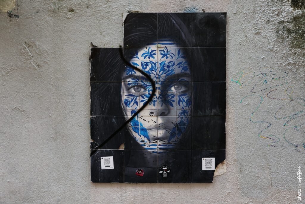 Street art de O Gringo montrant un visage féminin décoré de motifs azulejos bleus sur un mur urbain à Lisbonne.