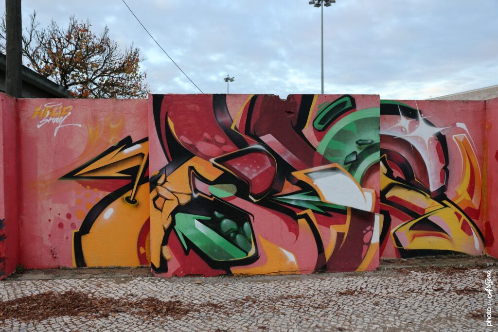 Street art de MosaikOne représentant un graffiti coloré et volumétrique peint sur un mur rose à Lisbonne.