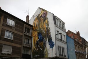 Fresque monumentale Jarus street art pêcheur en ciré jaune sur façade urbaine.