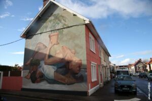 Fresque street art Artez montrant une femme en posture inversée tenant une plante sur un mur extérieur