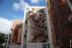 Street art de Guido Palmadessa à Boulogne-sur-Mer représentant deux figures masculines enlacées en style réaliste contemporain.
